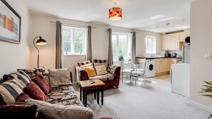 Una sala de estar moderna con sofá, una mesa de centro y un comedor. Hay una cocina con lavadora y refrigerador.