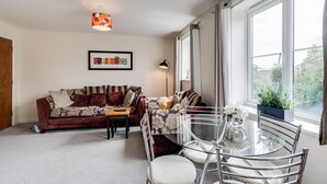 Una sala de estar acogedora con un sofá, una mesa de vidrio y vistas al verdor exterior.