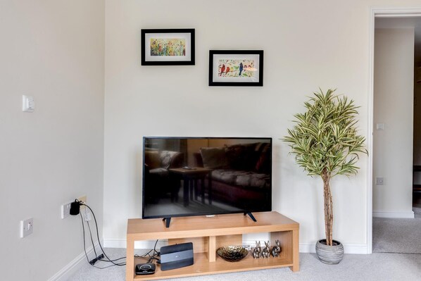 A living room with a TV on a wooden stand, two framed pictures on the wall, and a potted plant. - Modern 2 Bedroom Apartment in Popular Jericho (Oxford)