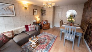 A cozy living room with a sofa, a coffee table with books, a dining table set for two, and a bookshelf. - A Very British Place to Stay - 3 Bedrooms Central (Oxford)