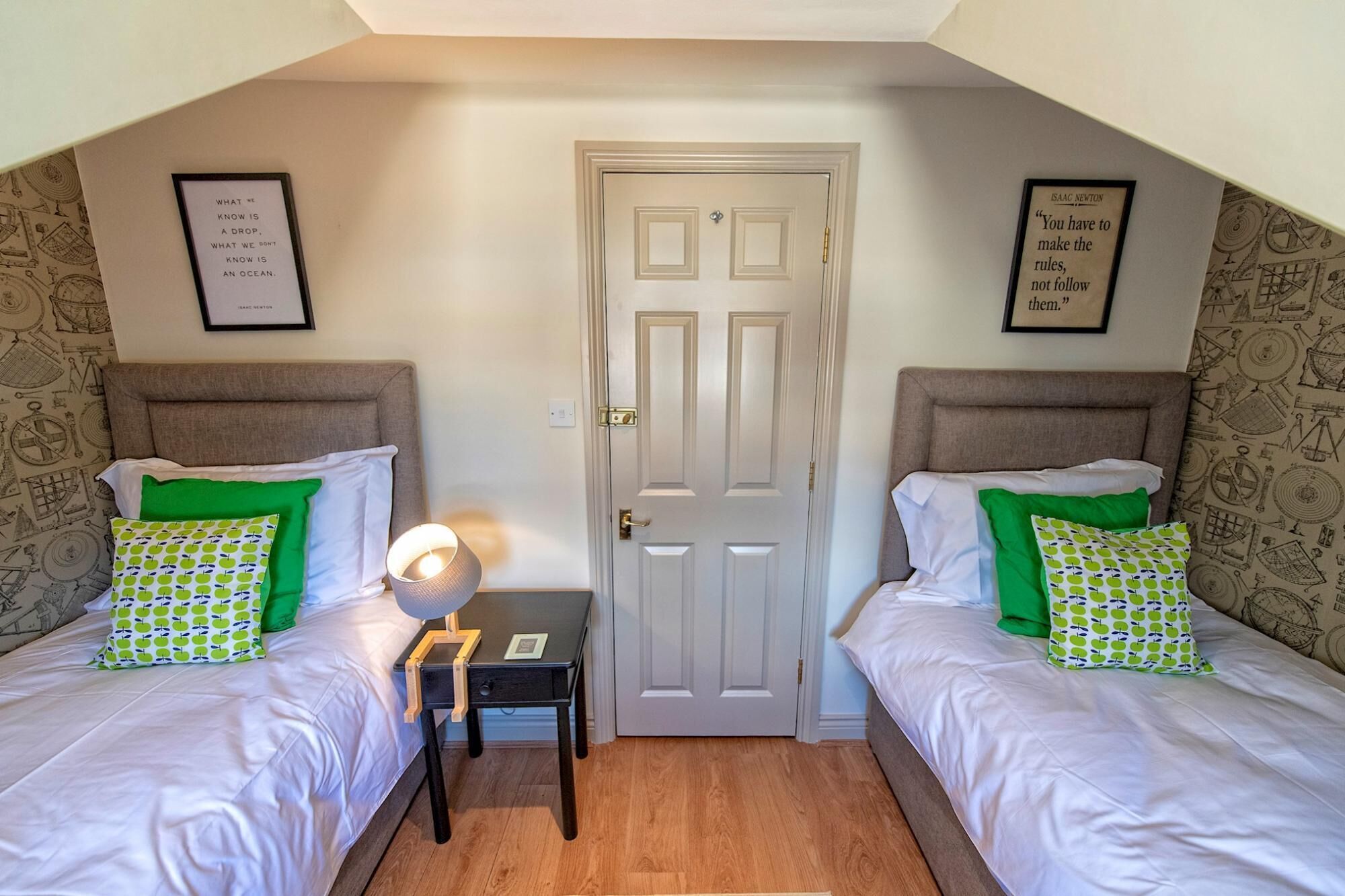 A room with two beds, a door, and two framed quotes on the walls.