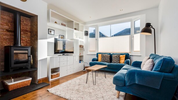 A modern living room with a fireplace, a blue sofa, a TV, and a large window. - Charming 3 BR House - Garden Parking Near CS Lewis Park (Oxford)
