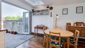 A dining area with a round wooden table and chairs, a small side table, a lamp, and a shelf with decorative items. - Charming 3 BR House - Garden Parking Near CS Lewis Park (Oxford)