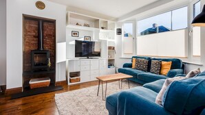 A modern living room with a fireplace, TV, and blue sofa. - Charming 3 BR House - Garden Parking Near CS Lewis Park (Oxford)