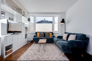 A modern living room with a large window, a dark blue sofa, a white entertainment unit, and a small wooden coffee table.