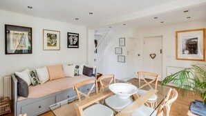 A modern living room with a sofa, a glass dining table, and chairs. There is a staircase leading to an upper level. - Headington Orchard - 3 Bedroom House Parking Garden (Oxford)