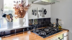 A modern kitchen with a black stove, a glass range hood, and a window with a view of greenery. - Headington Orchard - 3 Bedroom House Parking Garden (Oxford)