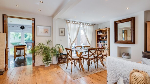 A spacious living area with a wooden floor, a glass dining table, and a white sofa. There is a bookshelf and a mirror on the wall. - Headington Orchard - 3 Bedroom House Parking Garden (Oxford)