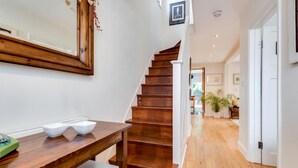 A wooden staircase with white railings, a wooden table with a bowl and a telephone, and a mirror on the wall. - Headington Orchard - 3 Bedroom House Parking Garden (Oxford)