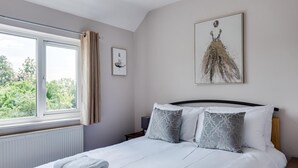 Un dormitorio con cama, almohadas, una ventana y una obra de arte en la pared.