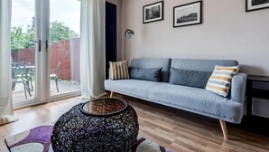 Una sala de estar moderna con un sofá gris, una mesa redonda de mimbre negro y una puerta de cristal que da a un patio.