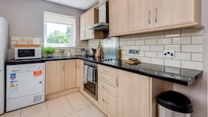 Una cocina moderna con armarios de madera clara, encimera negra, microondas, estufa y ventana que deja entrar luz natural.
