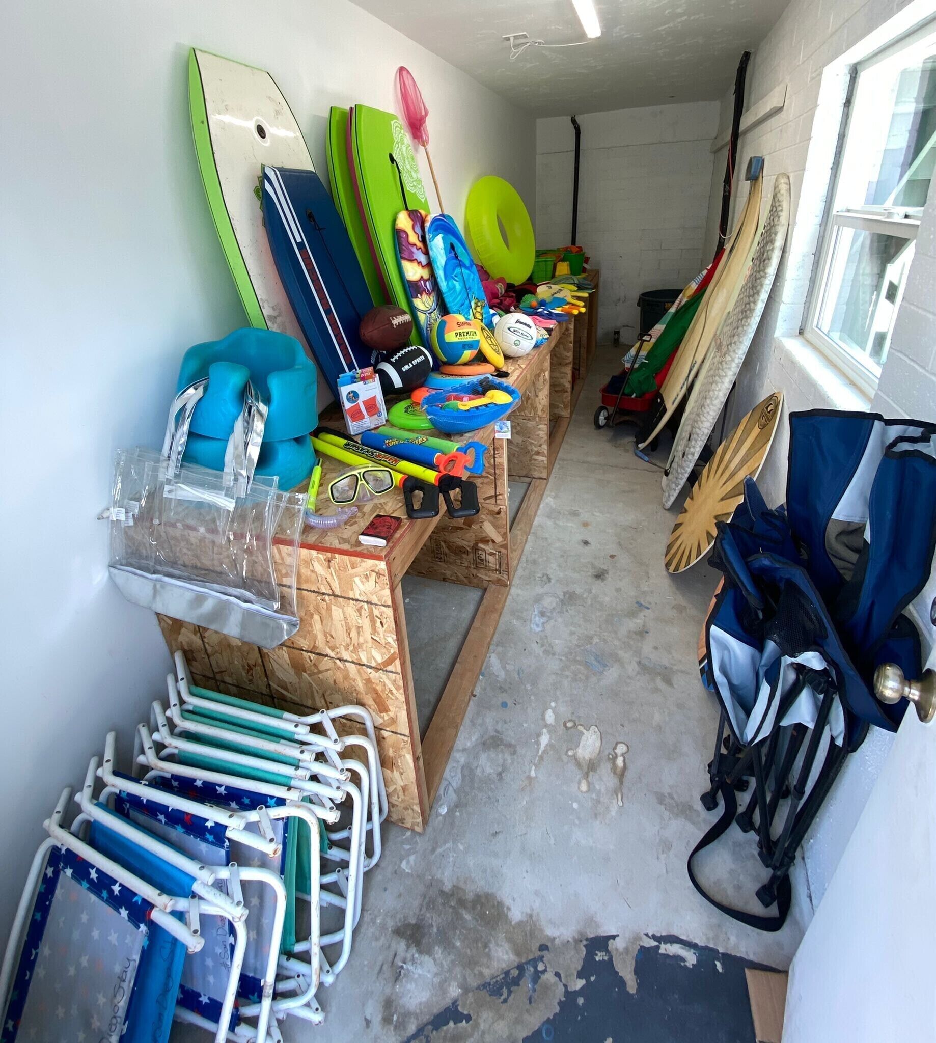 Un pasillo estrecho con varios equipos deportivos y juguetes, incluyendo una tabla de surf, un balón de baloncesto y un coche de juguete.