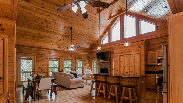 Una cabaña de madera espaciosa con comedor, sala de estar con sofá, cocina con barra y chimenea.