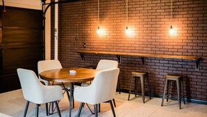 Un salón de conferencias con pared de ladrillo, una mesa redonda de madera, cuatro sillas blancas y dos taburetes de bar.