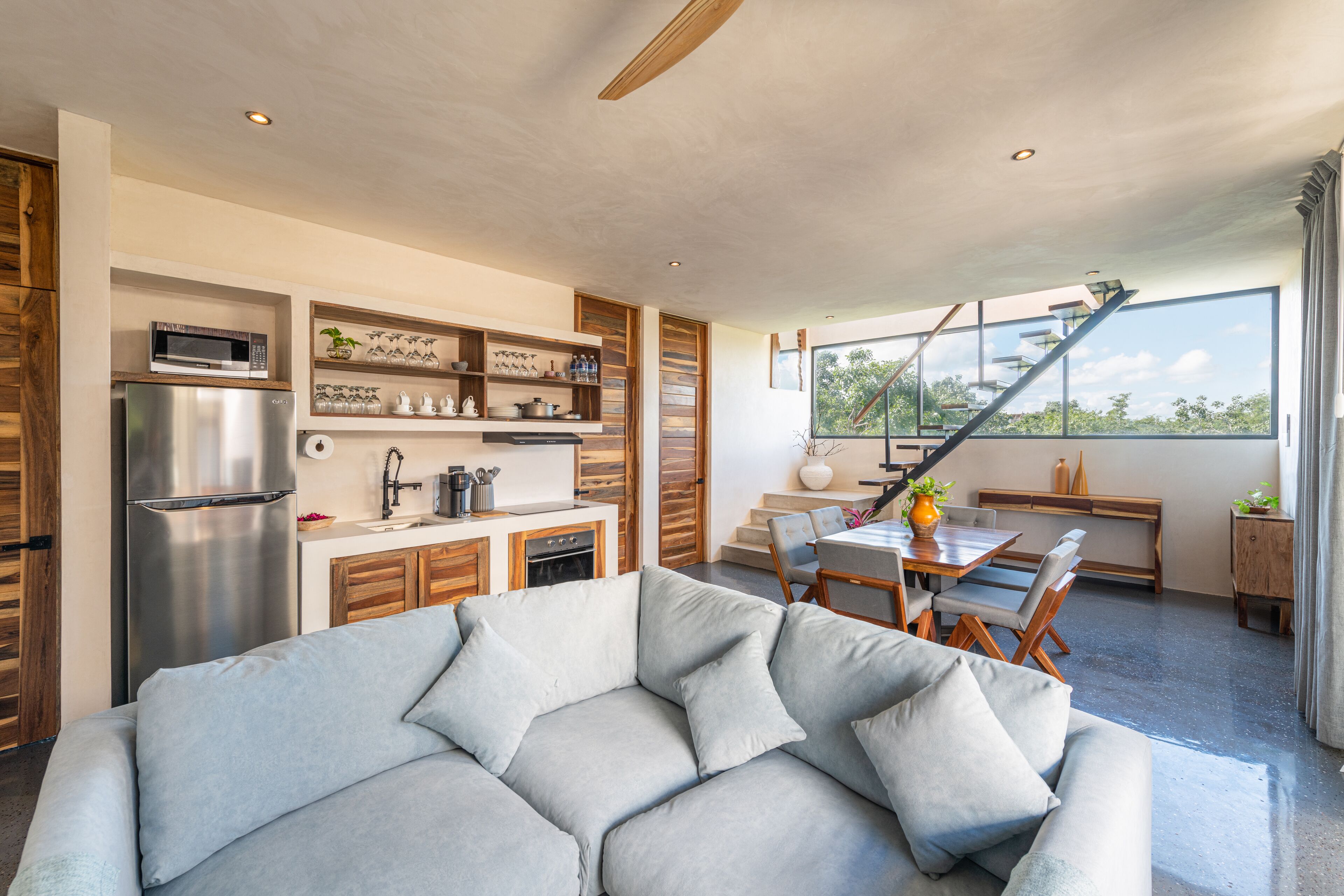 A modern kitchen with built-in appliances, a dining area with a wooden table and chairs, and a large window offering a view of the outdoors.