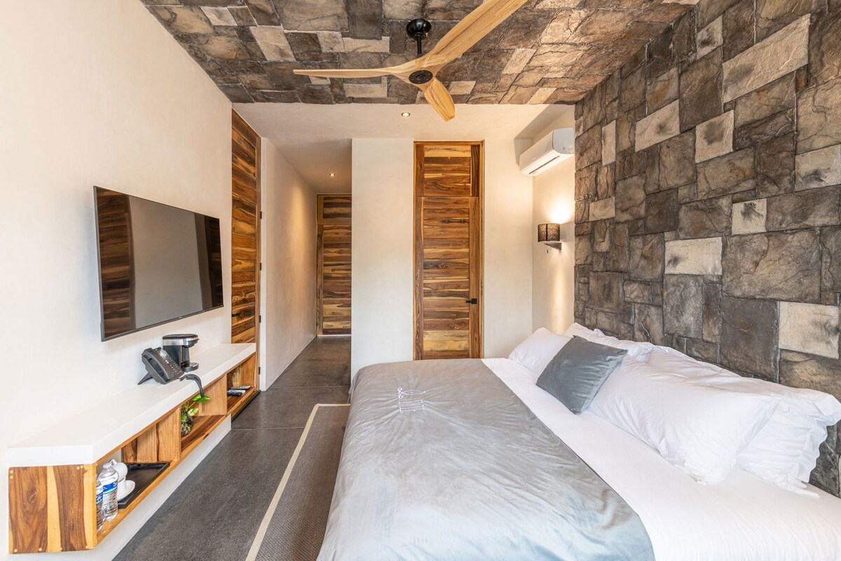 A modern bedroom with a bed, a TV, a wooden console, and a stone wall.