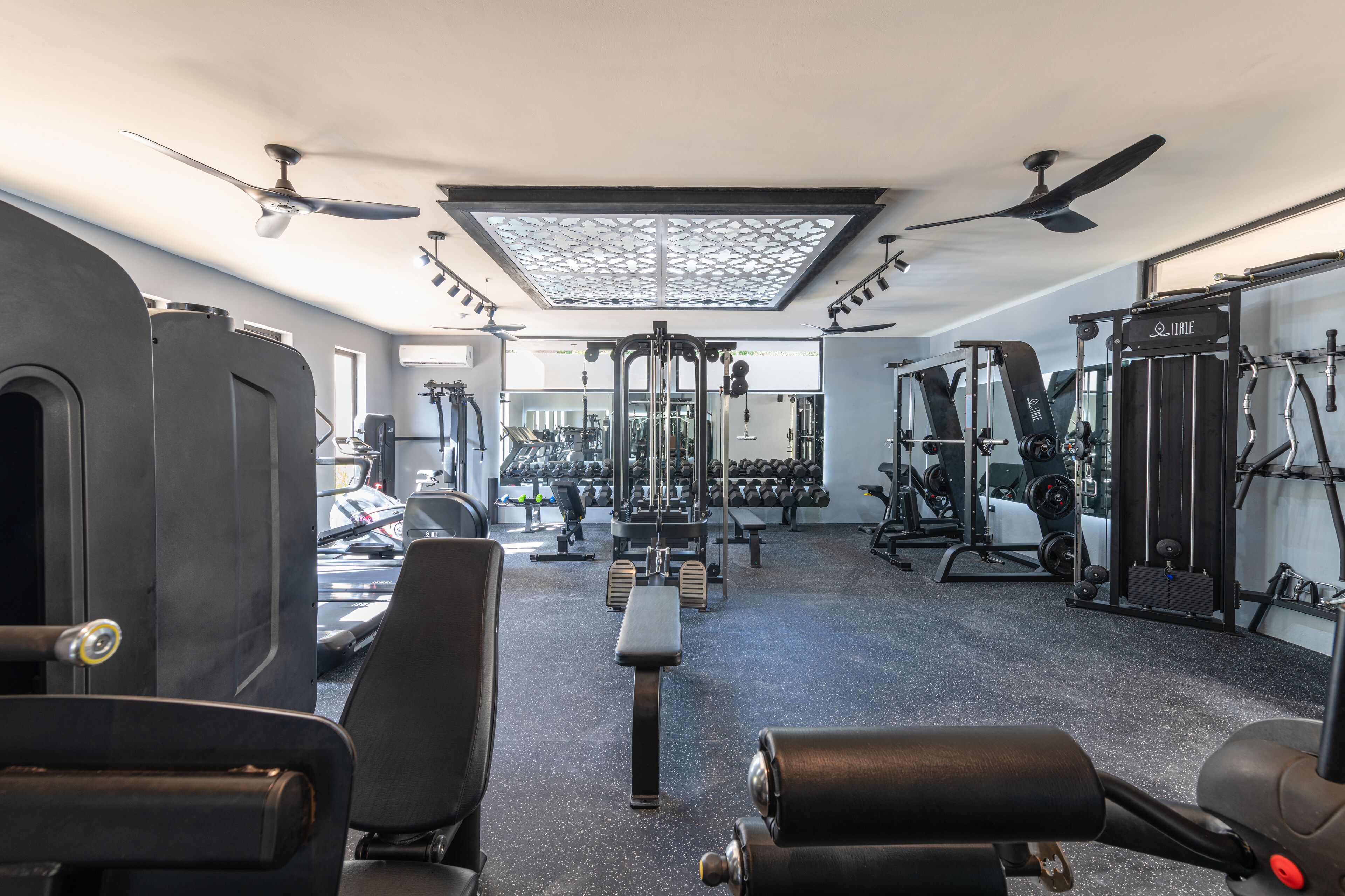 A gym with ceiling fans, exercise equipment, and a mirrored wall.