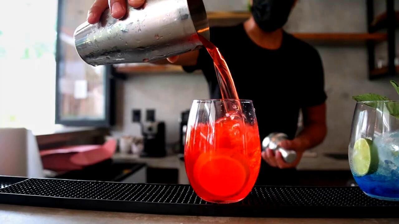 A bartender pouring a red drink into a glass.