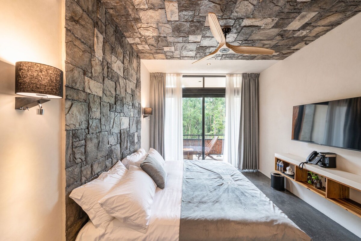 A bedroom with a stone wall, a bed, a TV, and a balcony with a view.
