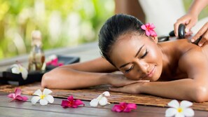 Un entorno de spa con una persona recibiendo un masaje, rodeada de flores y piedras de masaje.