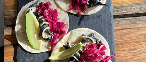 Three tacos on a slate board with lime wedges and a small clay pot.
