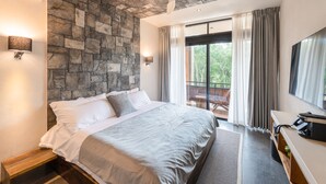 A modern bedroom with a stone wall, a large bed, a ceiling fan, a TV, and a balcony with curtains. - Irie Tulum  (Tulum)