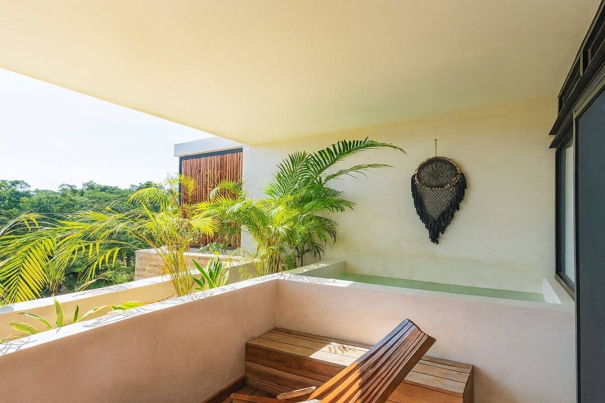 Ein Balkon mit einer Holzbank, einem gewebten Wandbehang und üppigem Grün im Hintergrund.
