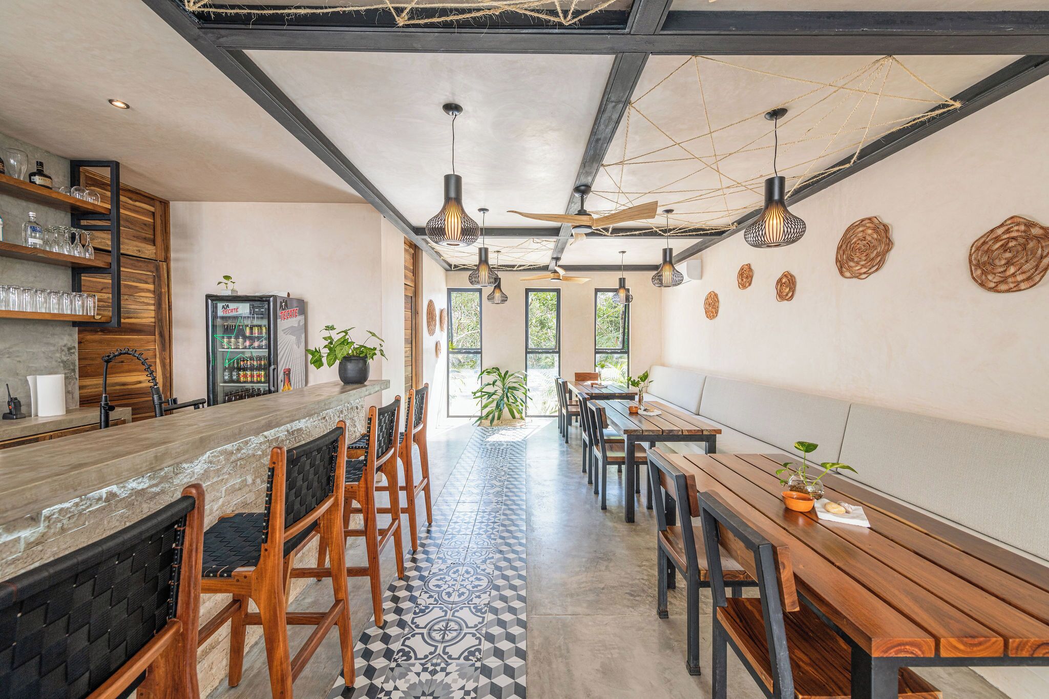 A modern cafe with a long counter, wooden chairs, and tables. There are hanging lights and a ceiling with exposed beams.