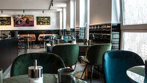 Un interior de restaurante moderno con sillas tapizadas de verde, mesas de mármol y obras de arte en las paredes.