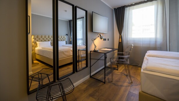 Una habitación de hotel con una cama, un escritorio con una silla, un televisor y un espejo grande.