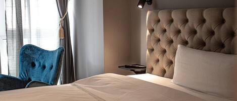 Una habitación de hotel con una cama grande, cabecero, mesita de noche y una silla.