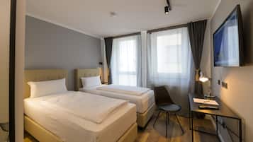 Habitación de hotel con dos camas, un escritorio con silla, un televisor y una ventana con cortinas.