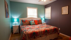 Une chambre à coucher avec un lit, deux lampes de chevet, un ventilateur de plafond et deux fenêtres.