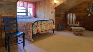 Quarto acolhedor de cabana com uma cama, uma cadeira, uma mesinha e um guarda-roupa.