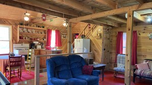 Interior acolhedor de uma cabana, com um sofá azul, paredes de madeira, uma área de cozinha e uma mesa de jantar.