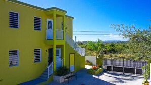 Un edificio amarillo con una escalera, una entrada protegida por una reja y un banco.