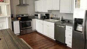 Cozinha moderna com armários brancos, eletrodomésticos de aço inoxidável, piso de madeira e lava-louças embutida.