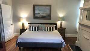 Quarto com cama, duas mesas de cabeceira com luminárias, um quadro na parede e uma porta.