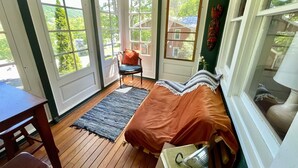 Une pièce confortable avec un lit, une chaise et une table. De grandes fenêtres offrent une vue sur l’extérieur.