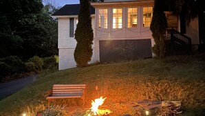 Une maison avec un foyer extérieur dans le jardin, un banc et une allée menant au garage.