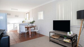 A modern living room with a flat-screen TV, a coffee table with decorative items, and a dining area with chairs and a table.