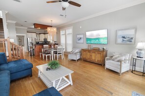 A spacious living room with a wooden floor, a blue sofa, a white coffee table, and a dining area with a wooden table and chairs.