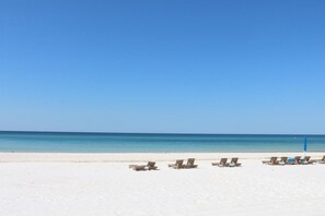 Ein Strand mit weißem Sand und blauem Himmel. Mehrere Liegestühle sind am Ufer aufgereiht.