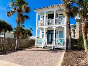 A two-story building with a balcony, a wooden fence, and palm trees. - Peach On The Beach 4 BR Beachfront Getaway, Rooftop Patio (Panama City Beach)