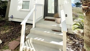 A two-story house with a white exterior, a black front door, and a small porch with steps. - Peach On The Beach 4 BR Beachfront Getaway, Rooftop Patio (Panama City Beach)