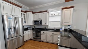 A modern kitchen with stainless steel appliances, white cabinetry, and a black granite countertop.