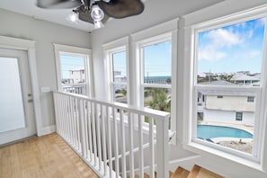 Un balcón con barandilla blanca, ventanas amplias y vista a una piscina y edificios.