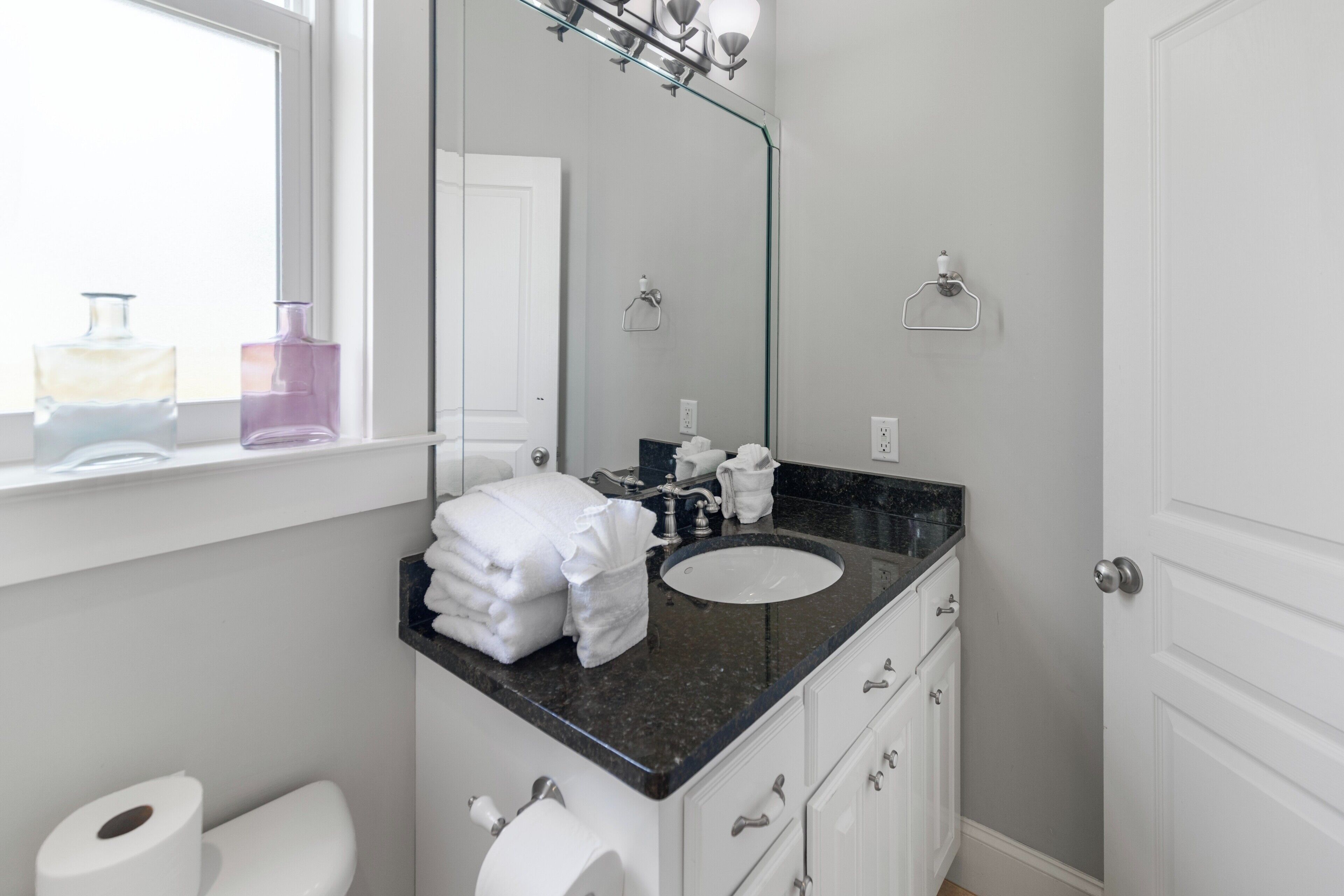 A bathroom with a white sink, a mirror, a window, and a toilet.
