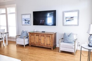 A living room with a wooden cabinet, two armchairs, a television, and framed artwork on the wall. - Peach On The Beach 4 BR Beachfront Getaway, Rooftop Patio (Panama City Beach)